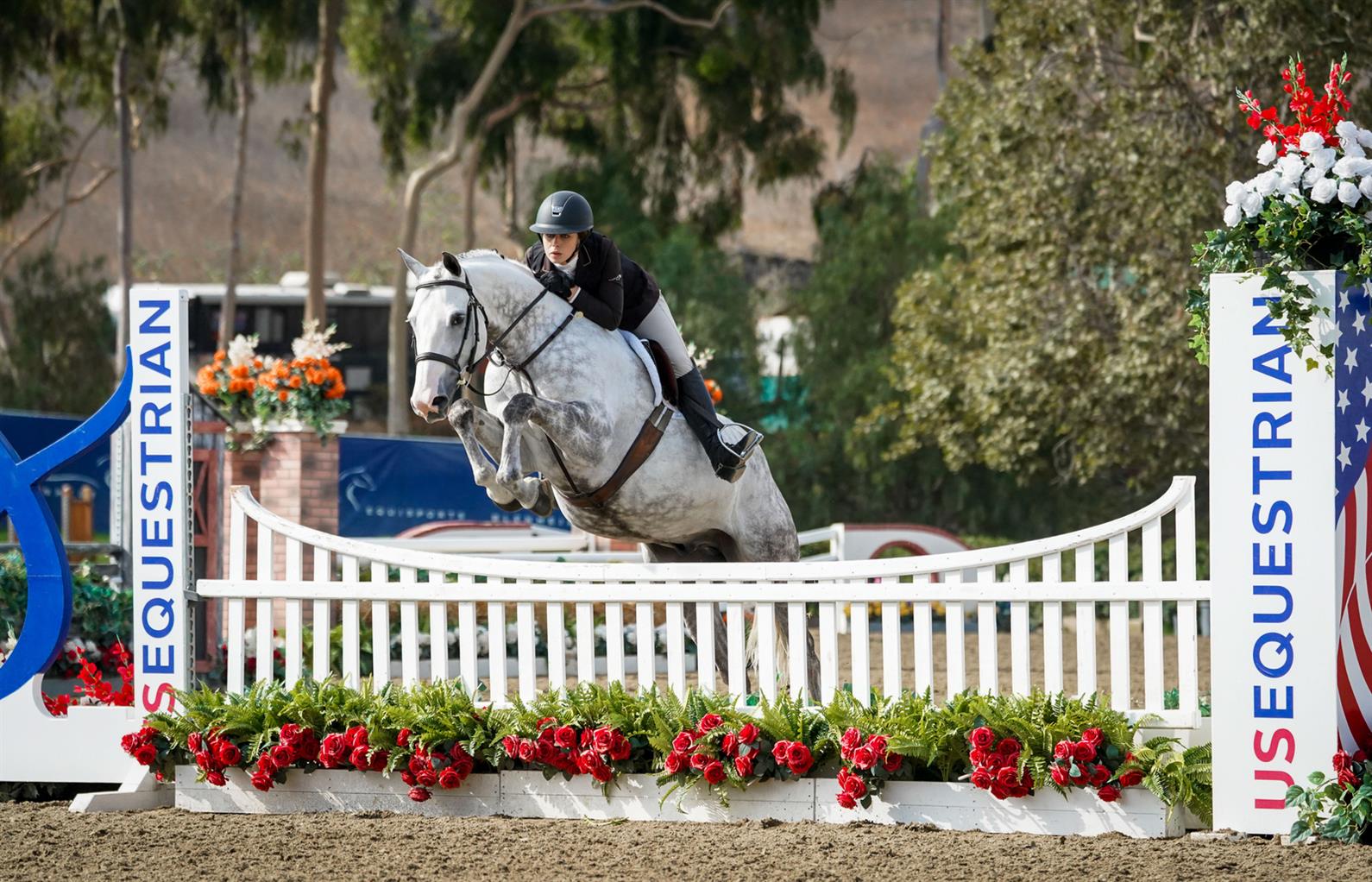 A gray horse clearing a jump with a junior rider at Junior Hunter Finals - West.